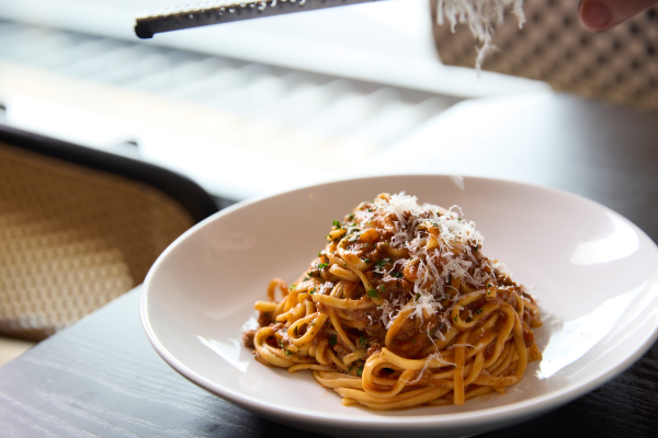 Plate of pasta topped with grated cheese, with a hand grating more cheese over it in a restaurant setting