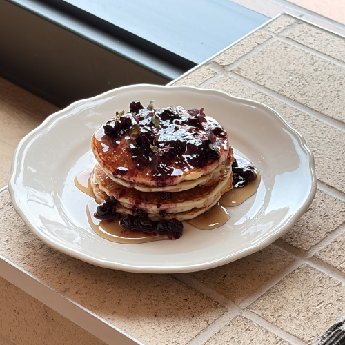 Stack of pancakes topped with berry compote and maple syrup, served on a plate